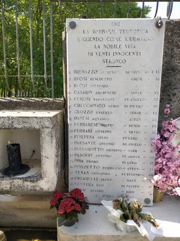 Monumento ai martiri di Villadose con nomi incisi in marmo e fiori decorativi in primo piano.