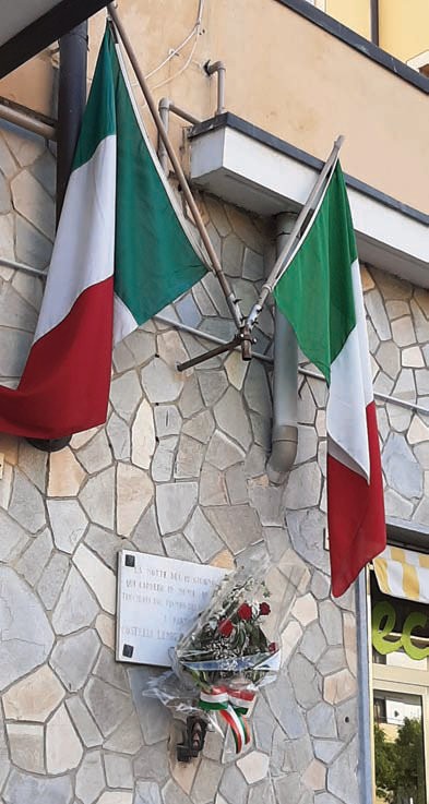 Lapide commemorativa dedicata a Costelli e Canelli, decorata con fiori e bandiere italiane.