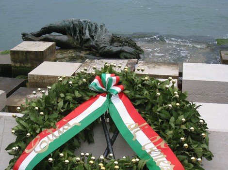 Monumento alla partigiana con una corona di alloro, sullo sfondo il mare e una scultura di una figura distesa.