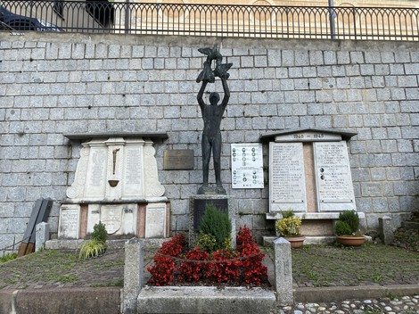 Monumento ai caduti di Castello Tesino, con statue e lapidi commemorative circondate da fiori.