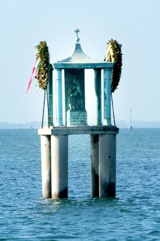 Monumento dedicato alle vittime del Giudecca, visibile in acqua con decorazioni floreali.