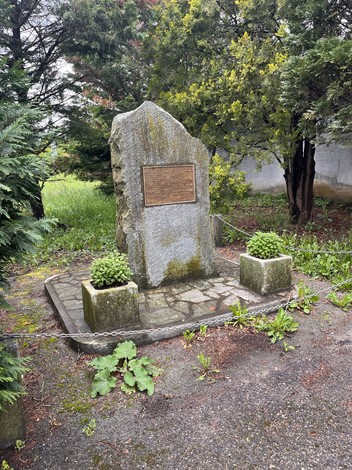 Monumento ai caduti circondato da vegetazione, con una stele e piccoli dettagli decorativi.