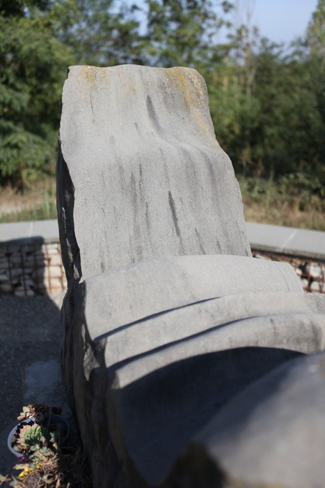 Monumento ai Martiri del Panaro, scultura in pietra con linee sinuose, circondato da verde. Atmosfera di rispetto e memoria.