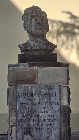 Monumento a Cavalli con busto e iscrizioni su base in pietra, situato in un contesto urbano.