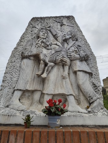 Monumento commemorativo con figure umane che esprimono dolore, floreale in omaggio ai caduti.