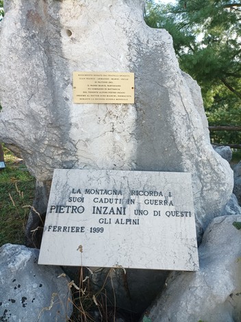 Monumento ai caduti in guerra, con targhe commemorative e un grande masso di pietra, immerso nella natura.