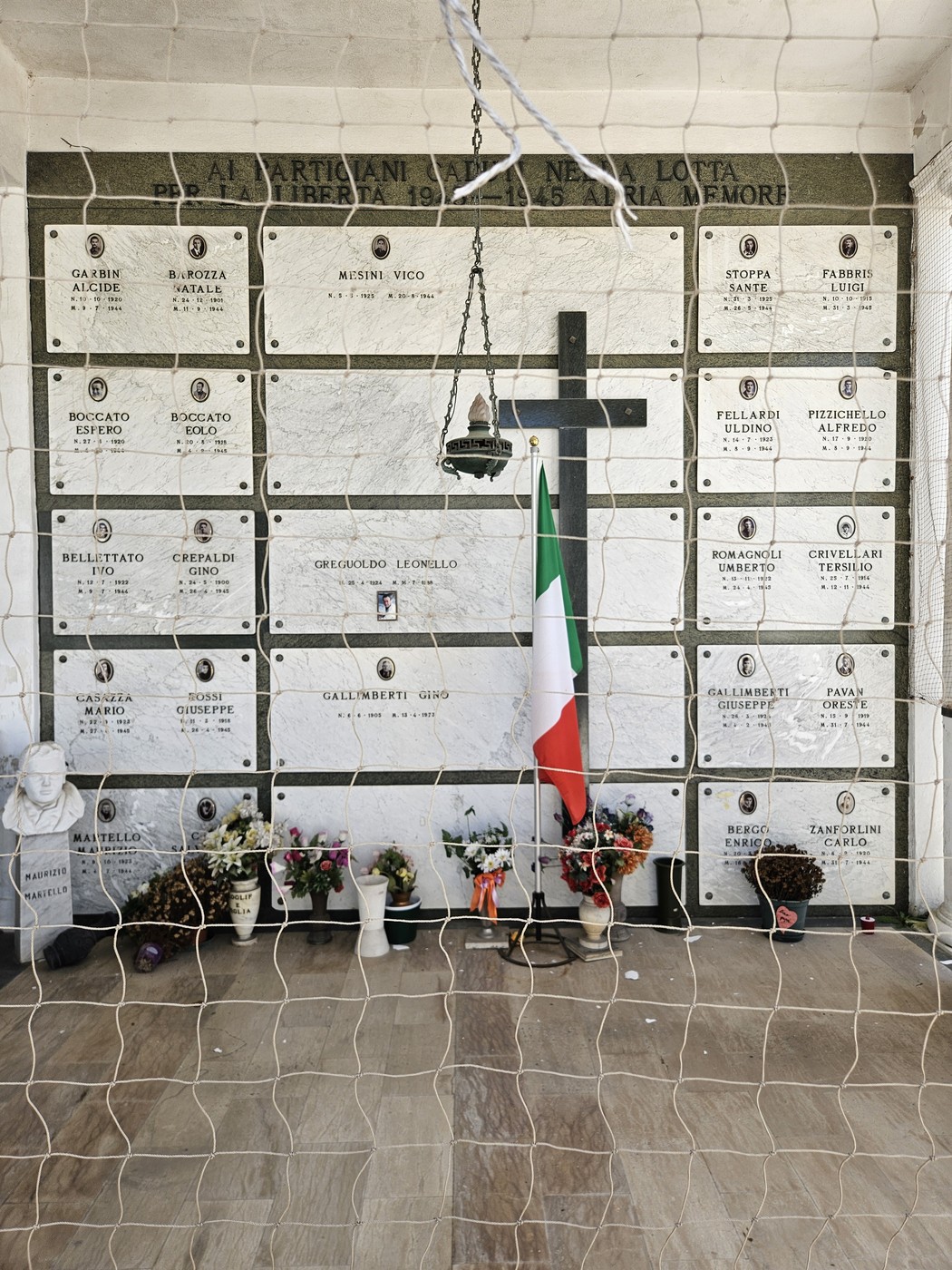 Sacrario dei Partigiani con pietre commemorative, una croce nera e decorazioni floreali, simbolo di memoria e resistenza.