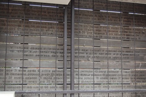 Una struttura moderna con pannelli di legno, decorati con testo incisivo, rappresenta il tema "L'ultimo treno".