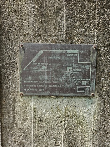 Placca di bronzo su superficie grezza, dedicata al Monumento alla Resistenza, con indicazioni e dettagli storici.