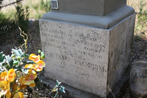 Cippo commemorativo dedicato a Gaetano Tacchini, con fiori e decorazioni, in un ambiente naturale.