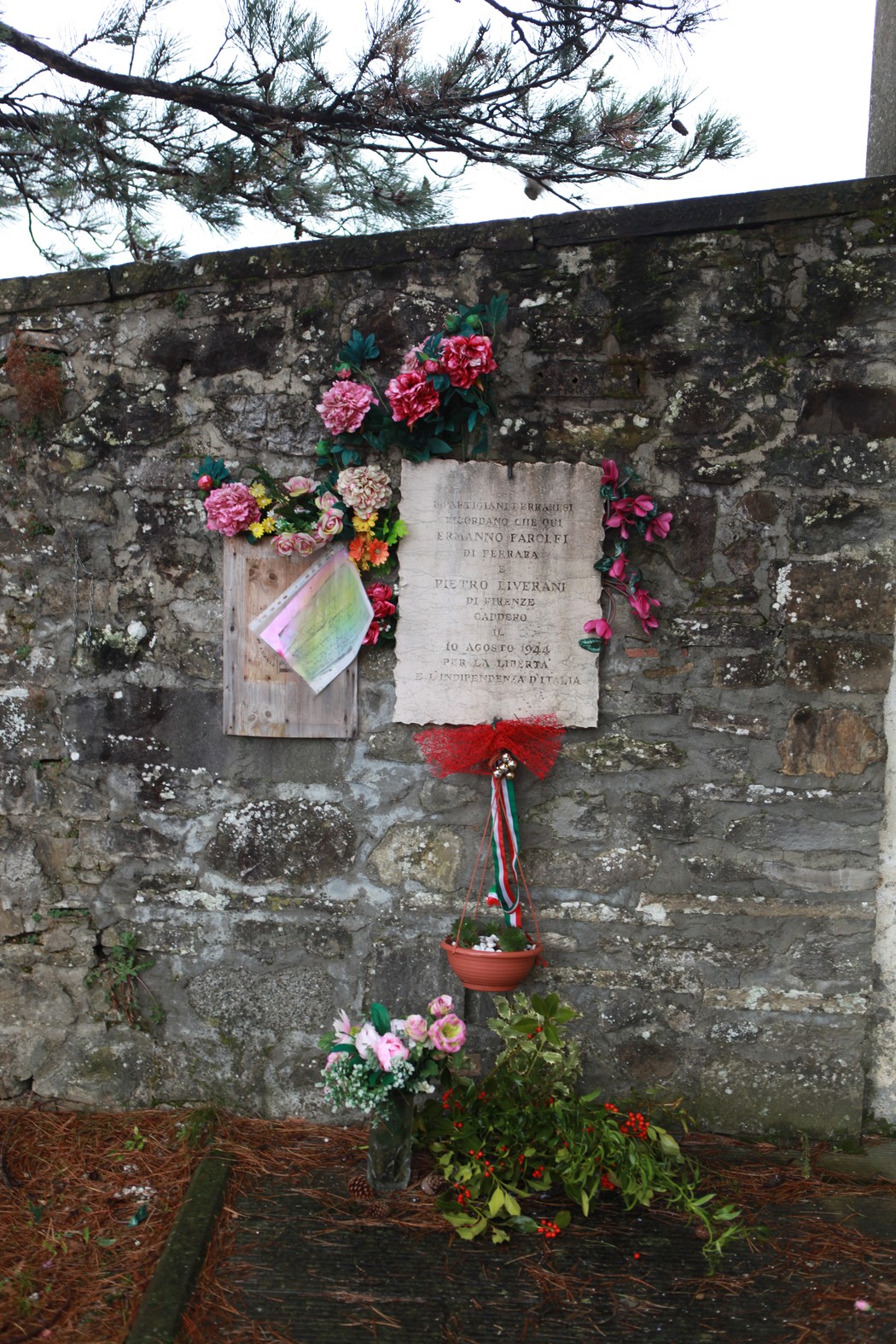 Lapide commemorativa decorata a Farolfi e Liverani, con fiori e omaggi sulla parete di pietra.