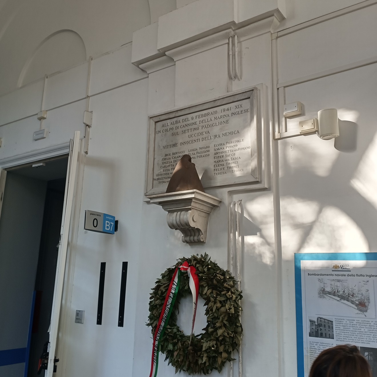 Lapide commemorativa all'interno di un'ospedale, con decorazioni floreali e riferimenti ai caduti.