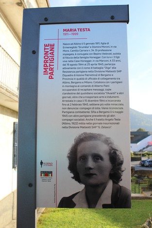 Immagine di una targa commemorativa con foto di Maria Testa e informazioni sulla sua eredità partigiana.