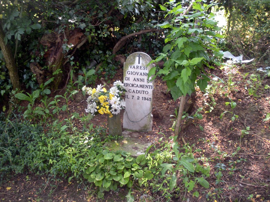 Cippo commemorativo a Varesi, dedicato a un giovane caduto nel 1945, circondato da vegetazione e fiori.