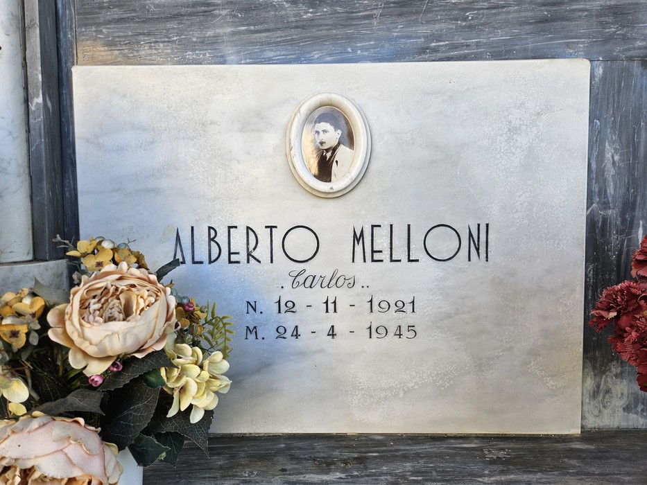 Lapide in marmo con ritratto ovale e iscrizione, decorata con fiori ai lati.