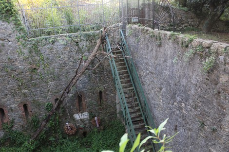 Struttura rustica con scale in metallo, circondata da mura in pietra e vegetazione, creando un'atmosfera di abbandono.