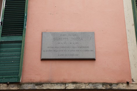 Lapide commemorativa dedicata a Giuseppe Dozza, situata su un muro colorato in un contesto urbano.