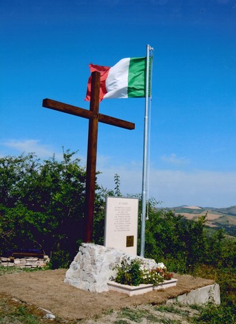 Monumento ai bersaglieri caduti a Poggio Scanno, con croce e bandiera italiana su sfondo di collina.