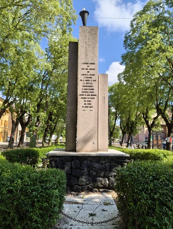 Monumento ai Caduti circondato da alberi, con colonne verticali e base in pietra, dedicato ai sacrifici dei soldati.
