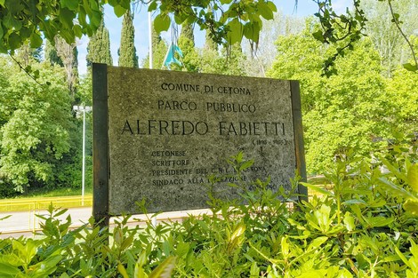 Insegna in pietra del parco pubblico Alfredo Fabietti, circondata da verde lussureggiante a Cetona.