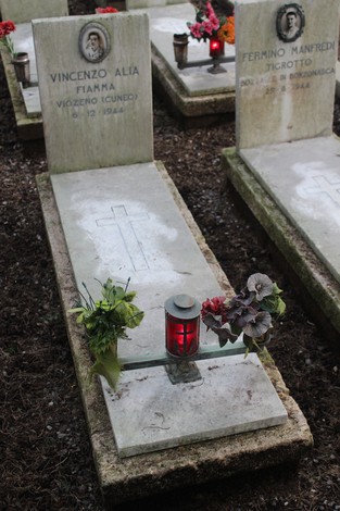 Tombe di caduti per la Libertà, con decorazioni floreali e candele, in un luogo di memoria e commemorazione.