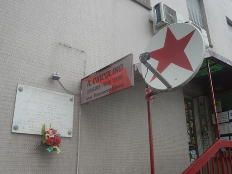 Lapide commemorativa ai caduti per la libertà a Porta Torino, con decorazioni floreali e insegne locali.