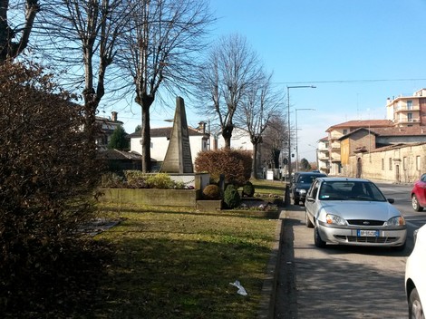 Monumento ad Arzani circondato da alberi e vegetazione, con veicoli in transito sulla strada vicina.