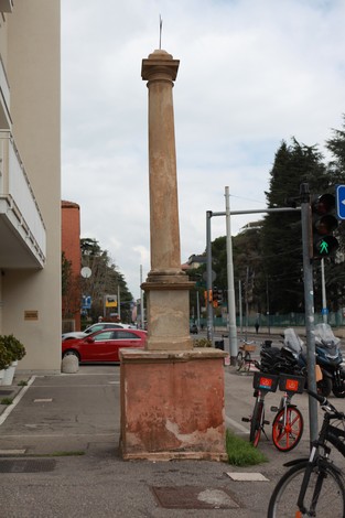 Lapide in pietra monumentale su basamento, situata in un contesto urbano, accanto a una strada.