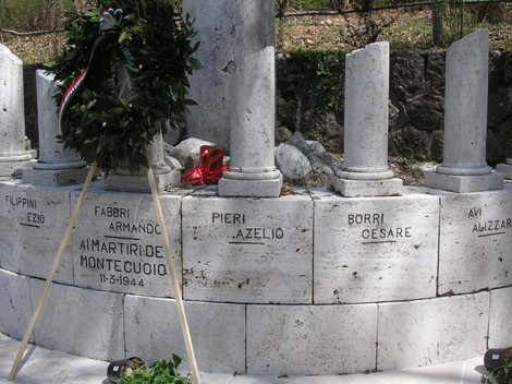 Monumento commemorativo ai caduti di Scalvaia, con nomi incisi su monumenti di pietra e una corona d'alloro.