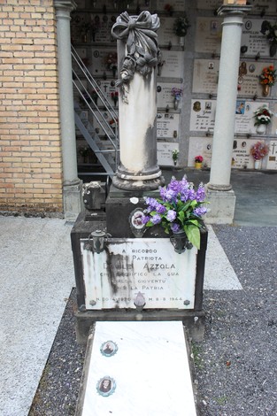 Cippo commemorativo ad Azzola, con decorazioni floreali e un'atmosfera di rispetto e memoriale.