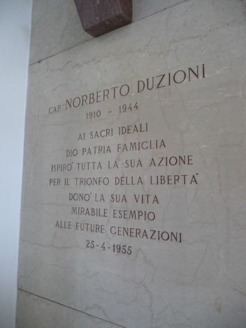 Lapide commemorativa dedicata a Norberto Duzioni, con testo inciso su pietra che celebra il suo sacrificio.