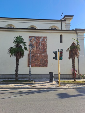 Bassorilievo che celebra la Liberazione, posizionato su una parete esterna, circondato da palme e semaforo.