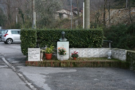 Monumento a Don Raglianti, commemorazione con busto e dedica in un'area curata tra piante e fiori.