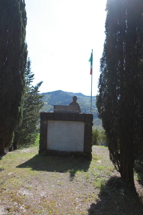 Monumento ai caduti di Purocielo, incorniciato da alberi e con vista panoramica sulle colline.