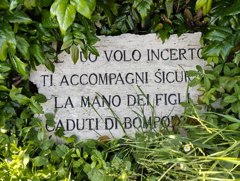 Monumento al Partigiano, con una dedica incisa su pietra, circondata da vegetazione rigogliosa.