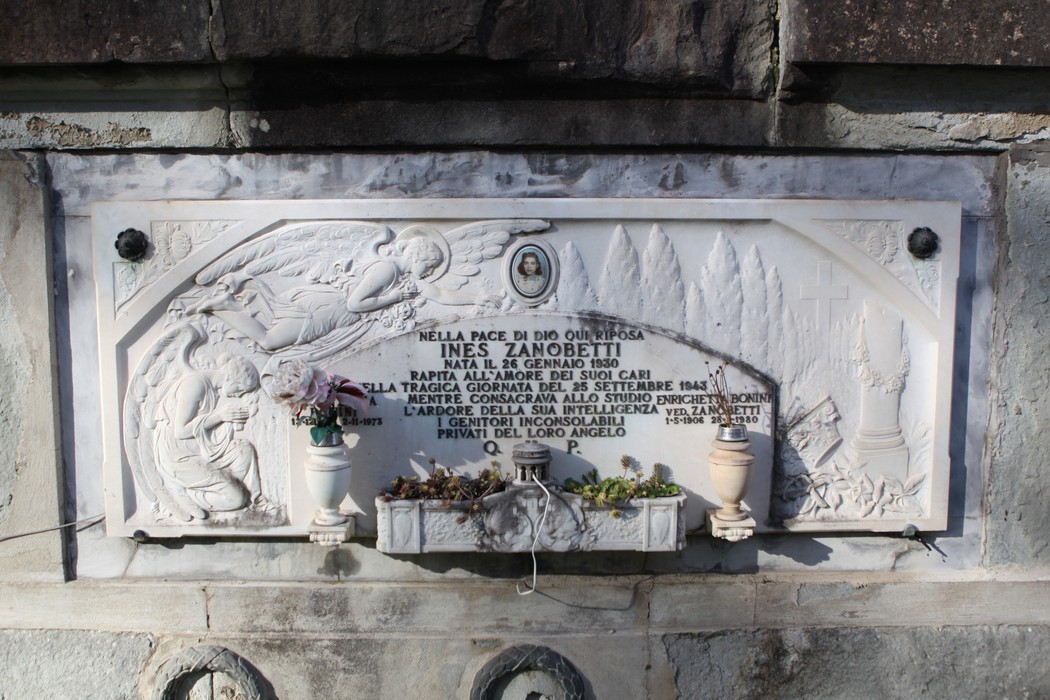 Targa commemorativa in memoria delle vittime dei bombardamenti con decorazioni floreali e simboli di ricordo.