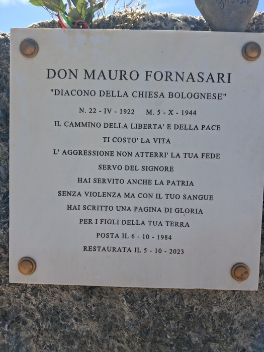 Cippo commemorativo dedicato a Don Mauro Fornasari, con iscrizioni che celebrano il suo servizio e i valori di libertà e pace.