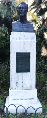 Monumento a Gastaldi con busto e base in marmo, circondato da vegetazione.