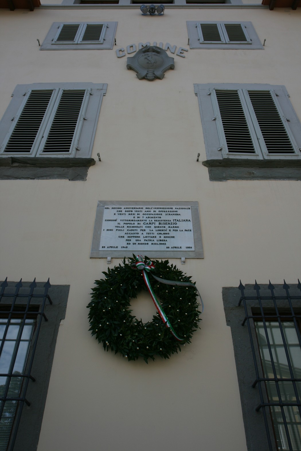 Lapide commemorativa con corona d'alloro su un edificio comunale, in ricordo di eventi significativi.