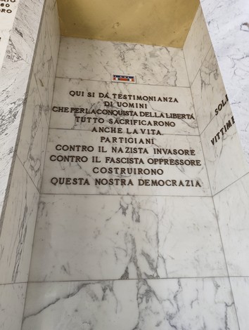 Sacrario dei caduti con iscrizioni commemorative su fondo marmoreo, onora la memoria dei sacrifici per la libertà.