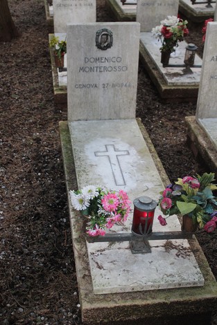 Tombe in un cimitero, con fiori e candele, dedicate ai caduti per la libertà. Atmosfera di rispetto e memoria.