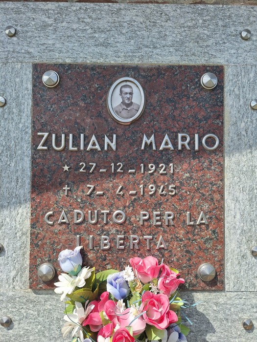 Monumento commemorativo in onore di Zulian Mario con targa e decorazioni floreali.