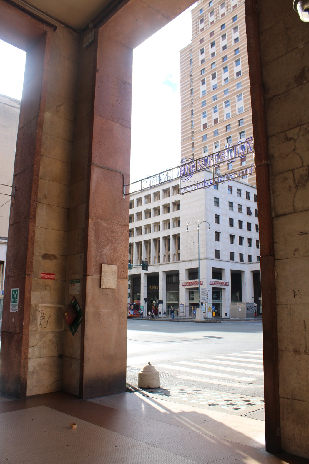 Vista architettonica di un ingresso, con un traforo che affaccia su una strada urbana e edifici moderni sullo sfondo.