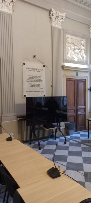Sala con lapidi storiche, arredo elegante e schermo per presentazioni, nel Municipio II.