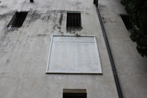 Stele commemorativa dedicata ai partigiani caduti, appesa a un muro in una zona urbana.