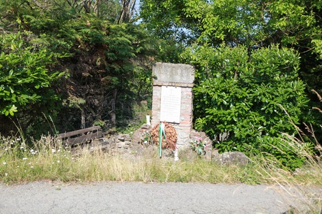 Monumento ai partigiani di Ca' di Bue, circondato da vegetazione e con una panchina vicina.