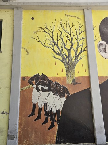 Murale a Piccinini con figure stilizzate, alberi secchi e colori vivaci, esprime un forte messaggio visivo.