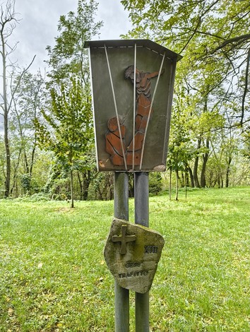Elementi della Via Crucis di Casaglia, con pannelli artistici in un contesto naturale e verdeggiante.