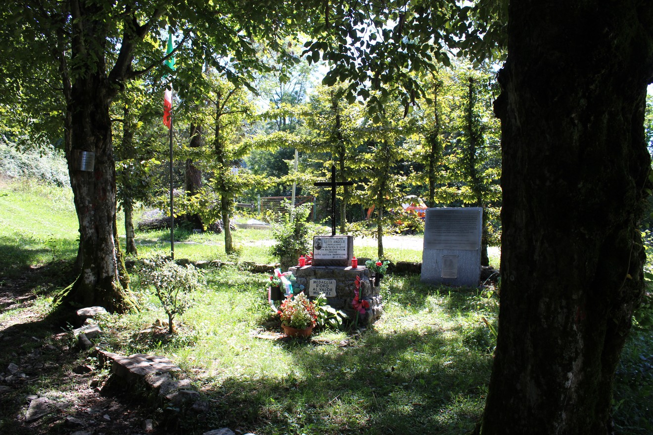 Monumento a Gotti circondato da alberi, fiori e bandiera italiana in un ambiente verde e tranquillo.