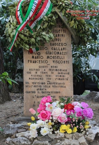 Cippo commemorativo dedicato ai caduti per la Libertà, adornato con fiori e un omaggio di foglie.